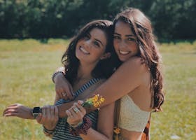 Two smiling sisters embracing in a sunlit park, enjoying a warm summer day together.